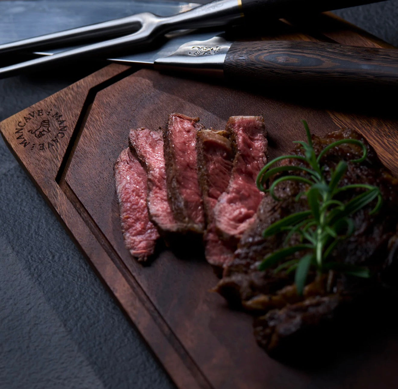 Sliced steak on a wooden cutting board with rosemary, set against a dark background. The Master´s Cutting Board