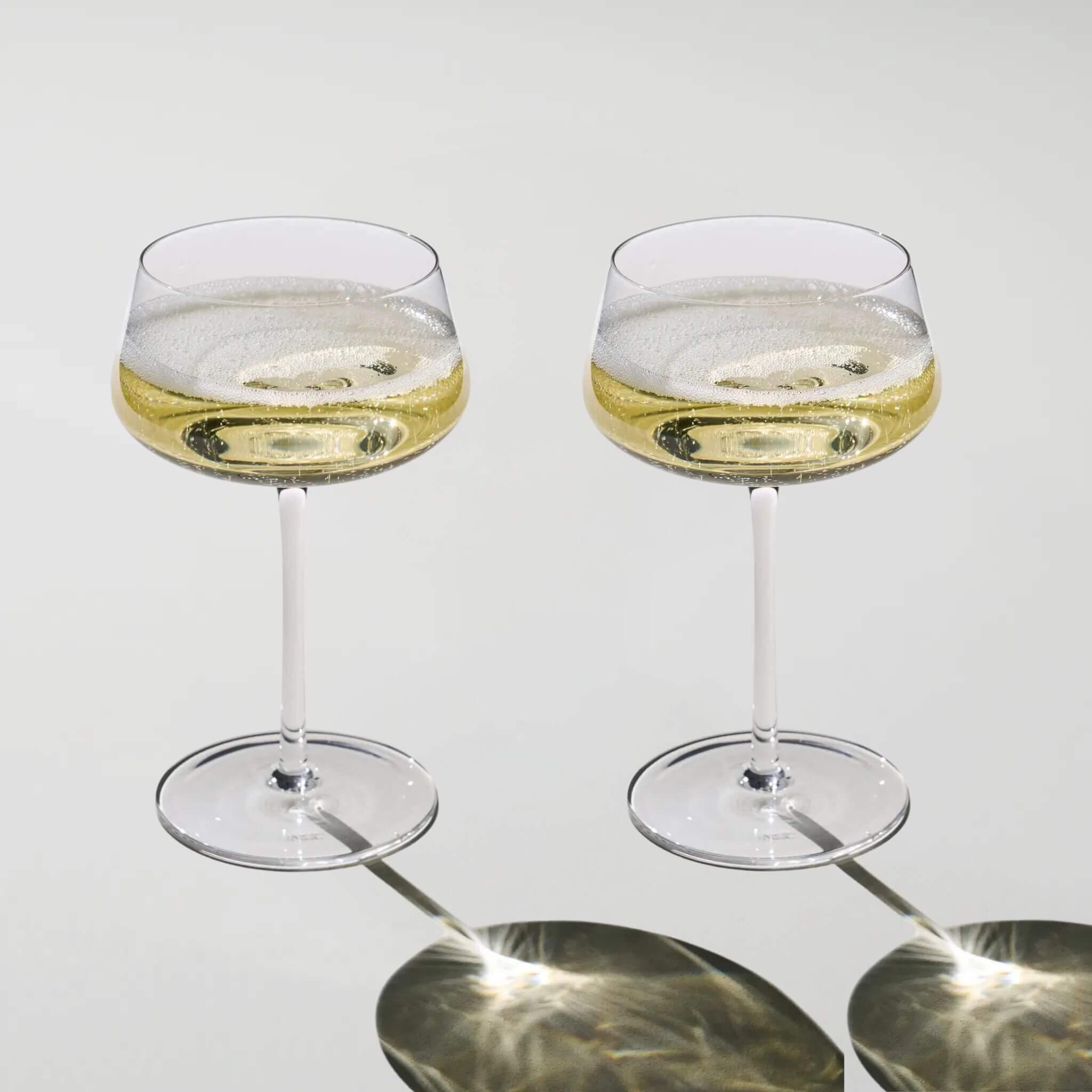 Two glasses of champagne on a reflective surface with a light gray background