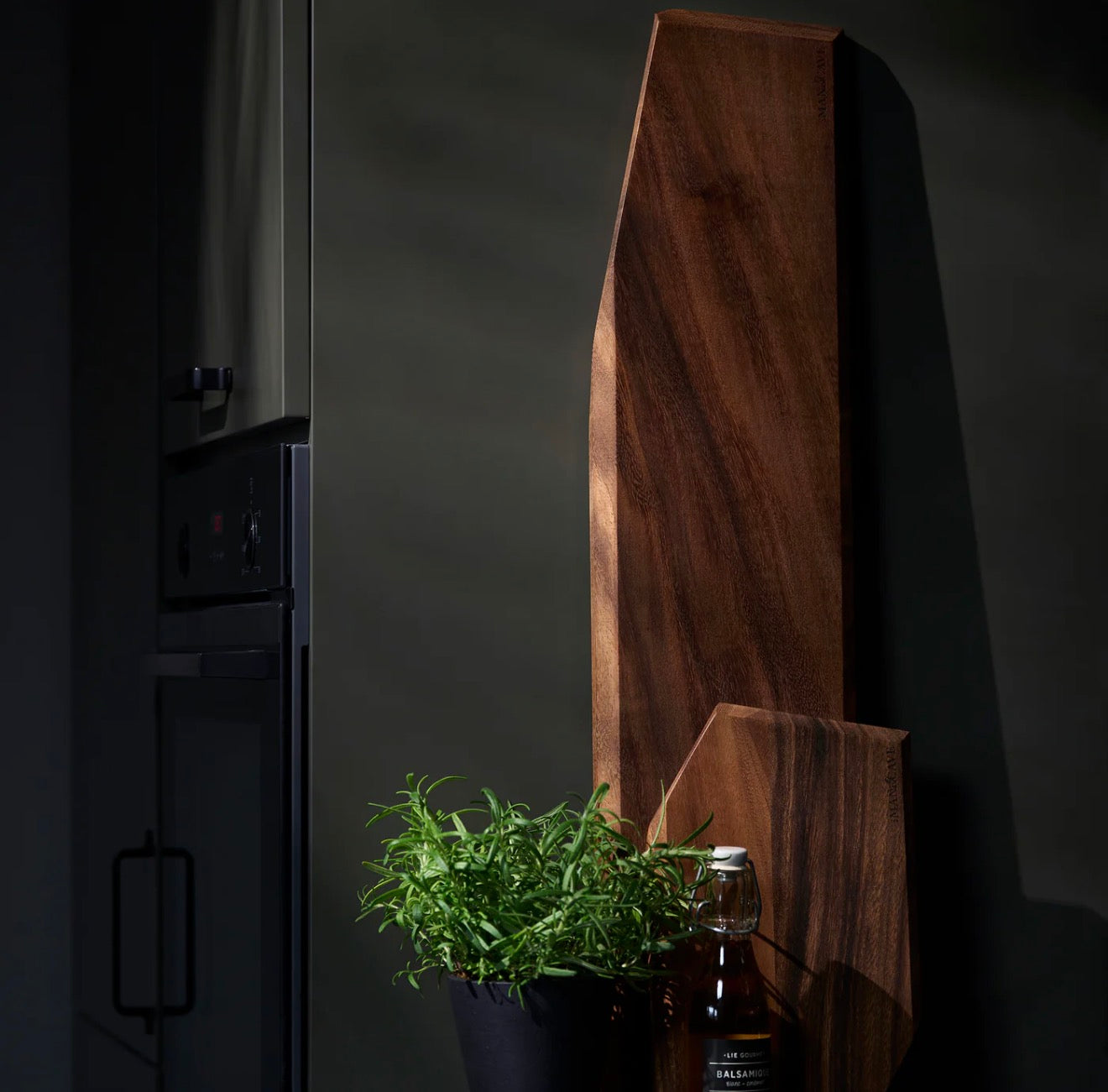 Dark wooden cutting board with a plant and bottle on a dark background The Gathering Board